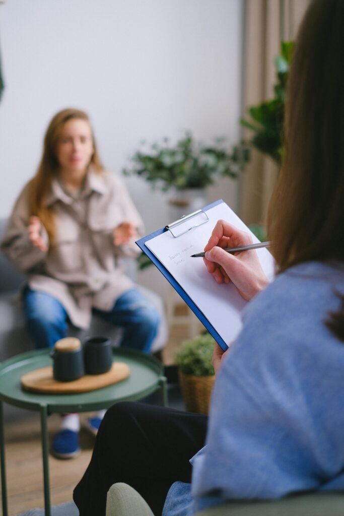 pexels-photo-7176036-7176036 Unrecognizable female psychologist taking notes on clipboard while listening to patient sitting on blurred background during psychotherapy consultation in office